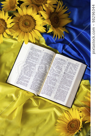 Bible (Holy Writ) and sunflowers on background of flag of Ukraine. 98296344