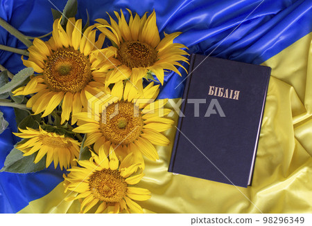 Bible (Holy Writ) and sunflowers on background of flag of Ukraine. Bible (Holy Writ) and sunflowers on background of flag of Ukraine. 98296349