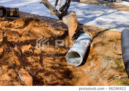 Worker working with tractor lift to install sewage pipes in ground is preparing install concrete pipes under ground to prevent subterranean flooding. 98296922