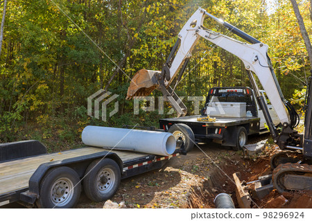 Work of worker who uses tractor to lift concrete sewage pipes in ground preparation for underground installation pipes 98296924