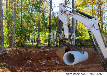 Using tractor worker is setting up concrete sewage pipes in preparation for installation of pipes underground. Using tractor worker is setting up concrete sewage pipes in preparation for installation of pipes underground. 98296925