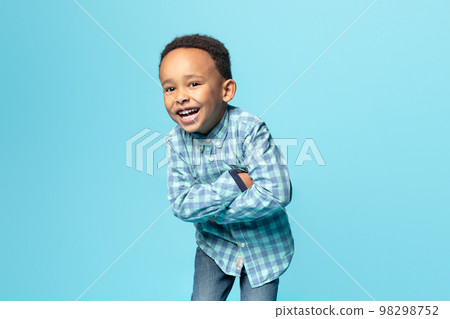 Portrait of cheerful little african american boy posing with folded arms and smiling at camera over blue background 98298752
