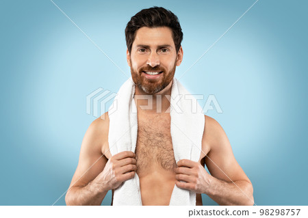 Portrait of happy shirtless bearded man with towel on neck posing on blue studio background and smiling at camera Portrait of happy shirtless bearded man with towel on neck posing on blue studio background and smiling at camera 98298757