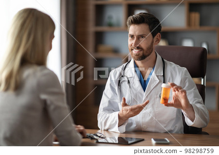 Smiling Doctor Man Demonstrating Prescribing Medications To Female Patient After Check Up Smiling Doctor Man Demonstrating Prescribing Medications To Female Patient After Check Up 98298759