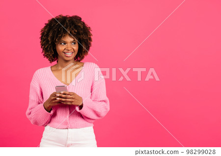 Happy millennial african american curly woman with braces in casual typing on phone looks at empty space 98299028