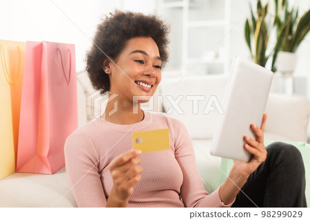 Smiling young mixed race female shopaholic with tablet, credit card checking financial account, use banking app 98299029