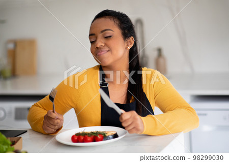 Happy pretty young african american woman chef in apron smelling fresh fish, enjoy dish, wont to eat Happy pretty young african american woman chef in apron smelling fresh fish, enjoy dish, wont to eat 98299030