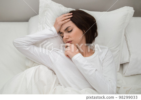 Top view of unhappy woman lying in bed, touching head Top view of unhappy woman lying in bed, touching head 98299033
