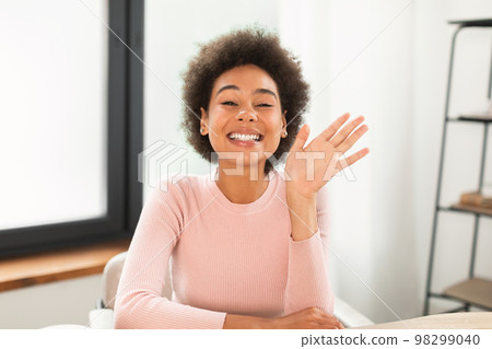 Cheerful young mixed race female manager waving hand, talking, shooting vlog, has video call at table 98299040