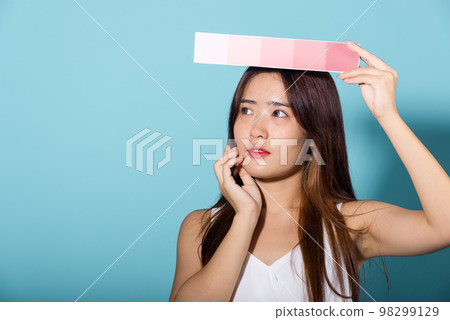 Asian beautiful young woman holding skin color scale paper studio shot isolated on blue background, Portrait of happy female hold color card under sun protection, skin beauty face 98299129