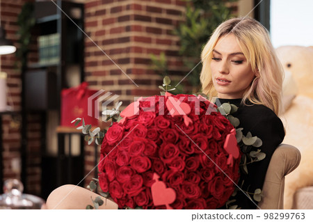 Beautiful woman holding flower bouquet in heart shaped box, enjoying celebrating valentine s day. Attractive blonde girlfriend with in black dress standing in living room filled with romantic presents Beautiful woman holding flower bouquet in heart shaped box, enjoying celebrating valentine s day. Attractive blonde girlfriend with in black dress standing in living room filled with romantic presents 98299763