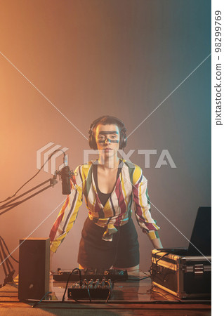 Modern artist standing at turntables and mixing equipment, using audio instruments or mixer to perform techno music. Serious musician with crazy make up doing remix with bass key and buttons. 98299769