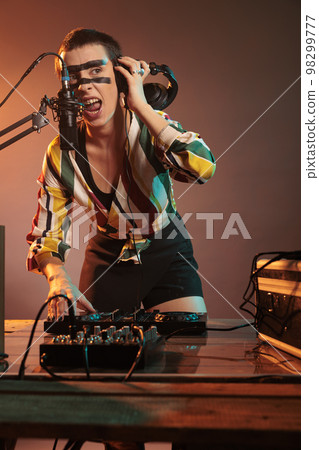 Musical performer mixing music at dj turntables, playing techno sounds with mixer and bass key in studio. Using headphones and microphone to create cool club performance, having crazy make up. Musical performer mixing music at dj turntables, playing techno sounds with mixer and bass key in studio. Using headphones and microphone to create cool club performance, having crazy make up. 98299777