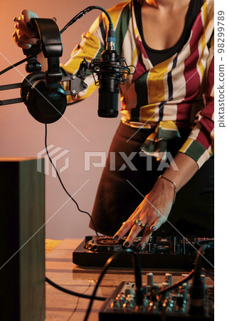 Woman musician using dj equipment and headphones to mix techno music and play electric remix on turntables, having fun with stereo instrument used for mixing sounds, bass volume. 98299789