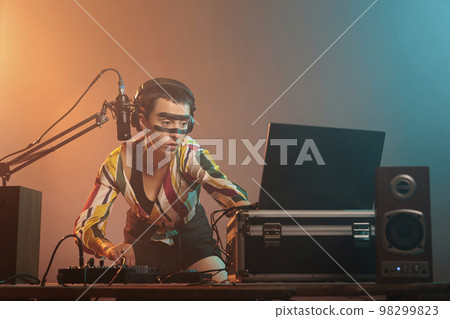 DJ woman using turntables to mix techno music, producing sounds at dj mixer with electronics and bass key. Woman working as artist doing remix stereo performance at nightclub in studio. 98299823