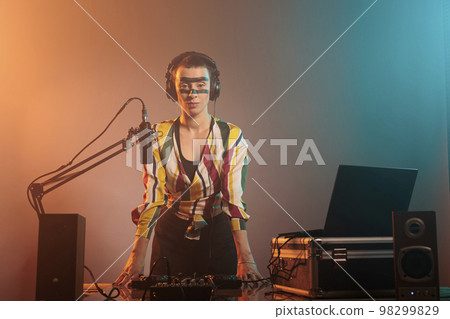 Musical artist with crazy make up having party to mix records and techno songs at tunrtables in studio. Using mixer to perform with audio equipment and stereo instrument, electronics. 98299829