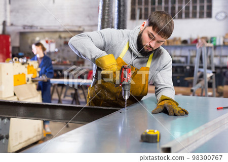Man engineer drilling metal sheet in workshop 98300767