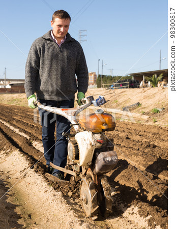 Gardener using motorized cultivator on the plantation 98300817
