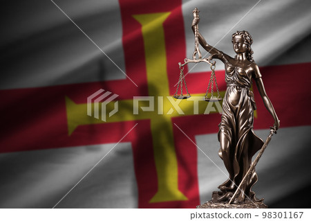 Guernsey flag with statue of lady justice and judicial scales in dark room. Concept of judgement and punishment Guernsey flag with statue of lady justice and judicial scales in dark room. Concept of judgement and punishment 98301167