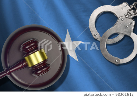 Somalia flag with judge mallet and handcuffs in dark room. Concept of criminal and punishment, background for judgement topics Somalia flag with judge mallet and handcuffs in dark room. Concept of criminal and punishment, background for judgement topics 98301612