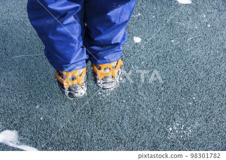 Feet of a child standing on an ice bubble wearing chain spikes Feet of a child standing on an ice bubble wearing chain spikes 98301782