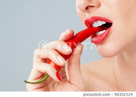 Woman with a red chili pepper between her teeth 98302524