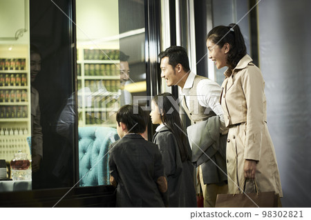 happy asian family with two children looking into a shop window in shopping mall happy asian family with two children looking into a shop window in shopping mall 98302821