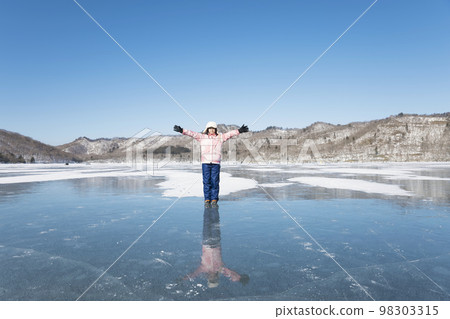 一個穿著冬裝的孩子戴著鏈釘站在湖冰上 一個穿著冬裝的孩子戴著鏈釘站在湖冰上 98303315