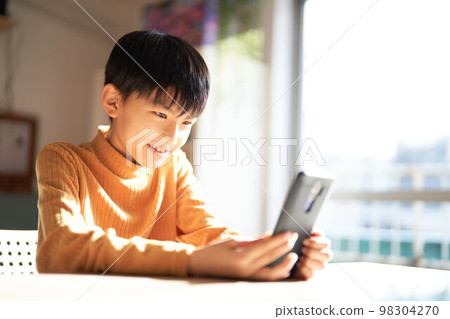 Elementary school boy looking at his smartphone with a smile Lifestyle image Elementary school boy looking at his smartphone with a smile Lifestyle image 98304270