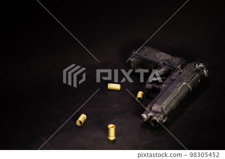 Handgun with 9mm shell casings on black background Handgun with 9mm shell casings on black background 98305452