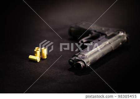 Handgun with 9mm shell casings on black background Handgun with 9mm shell casings on black background 98305455