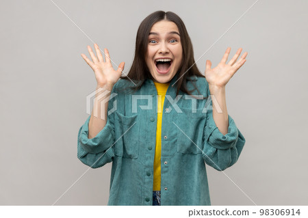 Portrait of positive attractive woman looking at camera with excitement, raised her arms, pleasant surprise, wearing casual style jacket. Indoor studio shot isolated on gray background. 98306914