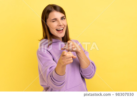 Happy satisfied woman pointing fingers on you looking at camera with toothy smile, congratulating with victory, wearing purple hoodie. Indoor studio shot isolated on yellow background. 98307030