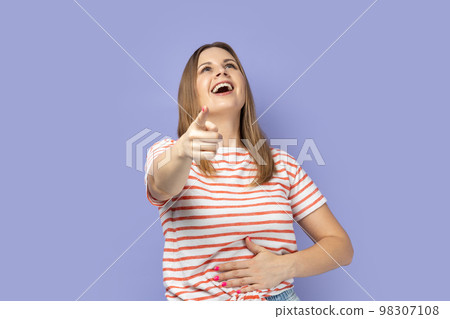 Ha ha, you're ridiculous. Portrait of woman wearing striped T-shirt pointing fingers to camera and laughing out loud, teasing funny friend appearance. Indoor studio shot isolated on purple background. Ha ha, you're ridiculous. Portrait of woman wearing striped T-shirt pointing fingers to camera and laughing out loud, teasing funny friend appearance. Indoor studio shot isolated on purple background. 98307108