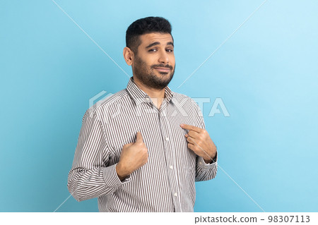 Portrait of bearded businessman pointing himself and looking selfish egoistic haughty, feeling proud of own achievement, wearing striped shirt. Indoor studio shot isolated on blue background. Portrait of bearded businessman pointing himself and looking selfish egoistic haughty, feeling proud of own achievement, wearing striped shirt. Indoor studio shot isolated on blue background. 98307113