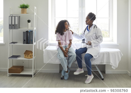 Caring doctor touches shoulder of excited teenage girl who is worried before medical examination. 98308760