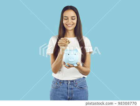 Portrait of happy woman who puts coin in piggy bank, saving money for purchase she dreams of. 98308770