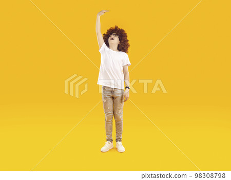 Funny cheerful little child standing on orange background and measuring his height 98308798