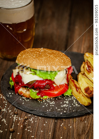 Homemade beef burger with mug of cold beer, baked potato, tomatoes, cheese, ketchup on wooden table Homemade beef burger with mug of cold beer, baked potato, tomatoes, cheese, ketchup on wooden table 98309055