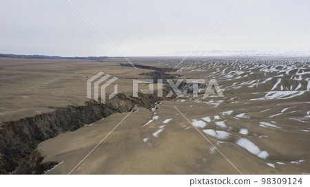 A crack in the ground with a view of snowy hills A crack in the ground with a view of snowy hills 98309124