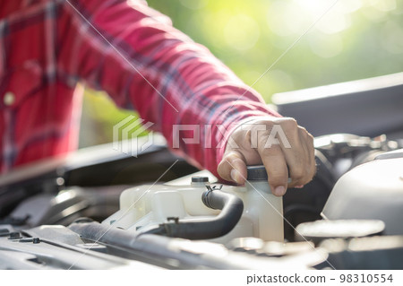 Man opening cap of car radiator to checking up the engine before start the trip. Car maintenance or check up concept Man opening cap of car radiator to checking up the engine before start the trip. Car maintenance or check up concept 98310554