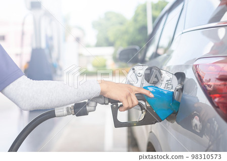 Hand of refueling worker are filling fuel to car in Petrol station. Focus on fuel nozzle and blur day light background 98310573