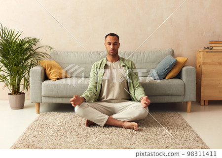Calm Man Meditating Home. Multiracial Guy Sitting In Lotus Pose Practicing Yoga Calm Man Meditating Home. Multiracial Guy Sitting In Lotus Pose Practicing Yoga 98311411