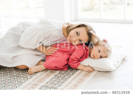 Mother and her little daughter are lying on a pillow on the floor, spending their free time together 98313939