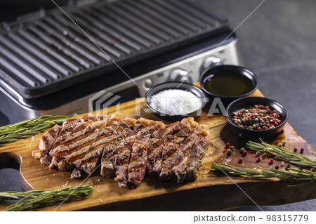 ribeye steak on wooden board with spices and electric grill 98315779