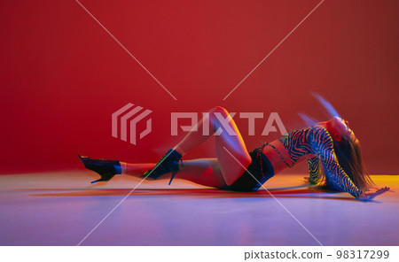 Passion, femininity. Portrait of young girl dancing heels dance over red background in neon with mixed light. Concept of modern dance style Passion, femininity. Portrait of young girl dancing heels dance over red background in neon with mixed light. Concept of modern dance style 98317299