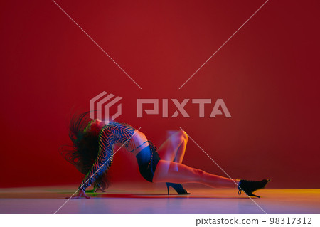 Feminine performance. Portrait of young girl dancing heels dance over red background in neon light. Concept of modern dance style 98317312