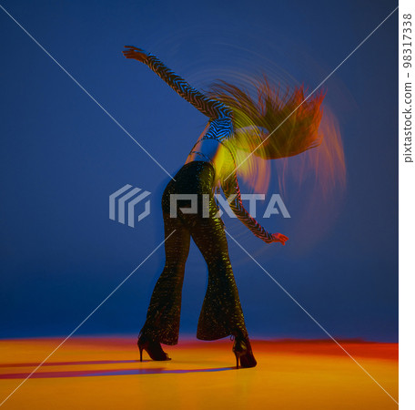 Clubbing. Portrait of young girl dancing heels dance in stylish clothes over blue background in neon with mixed lights. Concept of modern dance style 98317338