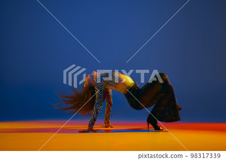 Flexibility and passion. Young girl dancing heels dance in stylish clothes over blue background in neon with mixed lights. Concept of modern dance style 98317339