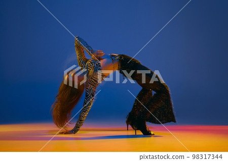 Flexible move. Young girl dancing heels dance in stylish clothes over blue background in neon with mixed lights. Concept of modern dance style Flexible move. Young girl dancing heels dance in stylish clothes over blue background in neon with mixed lights. Concept of modern dance style 98317344